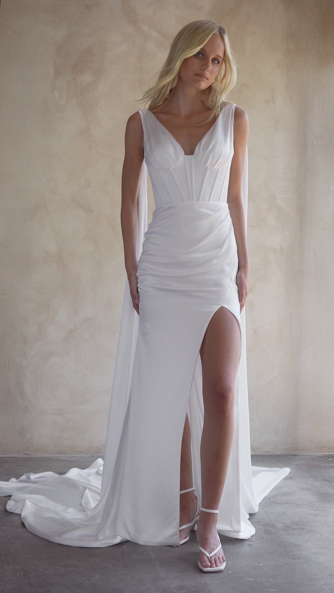 Video of the Jani satin wedding dress by the bryde. featuring exposed boning bodice with thigh high split and satin wings which can be wrapped around the neck for a modern look.